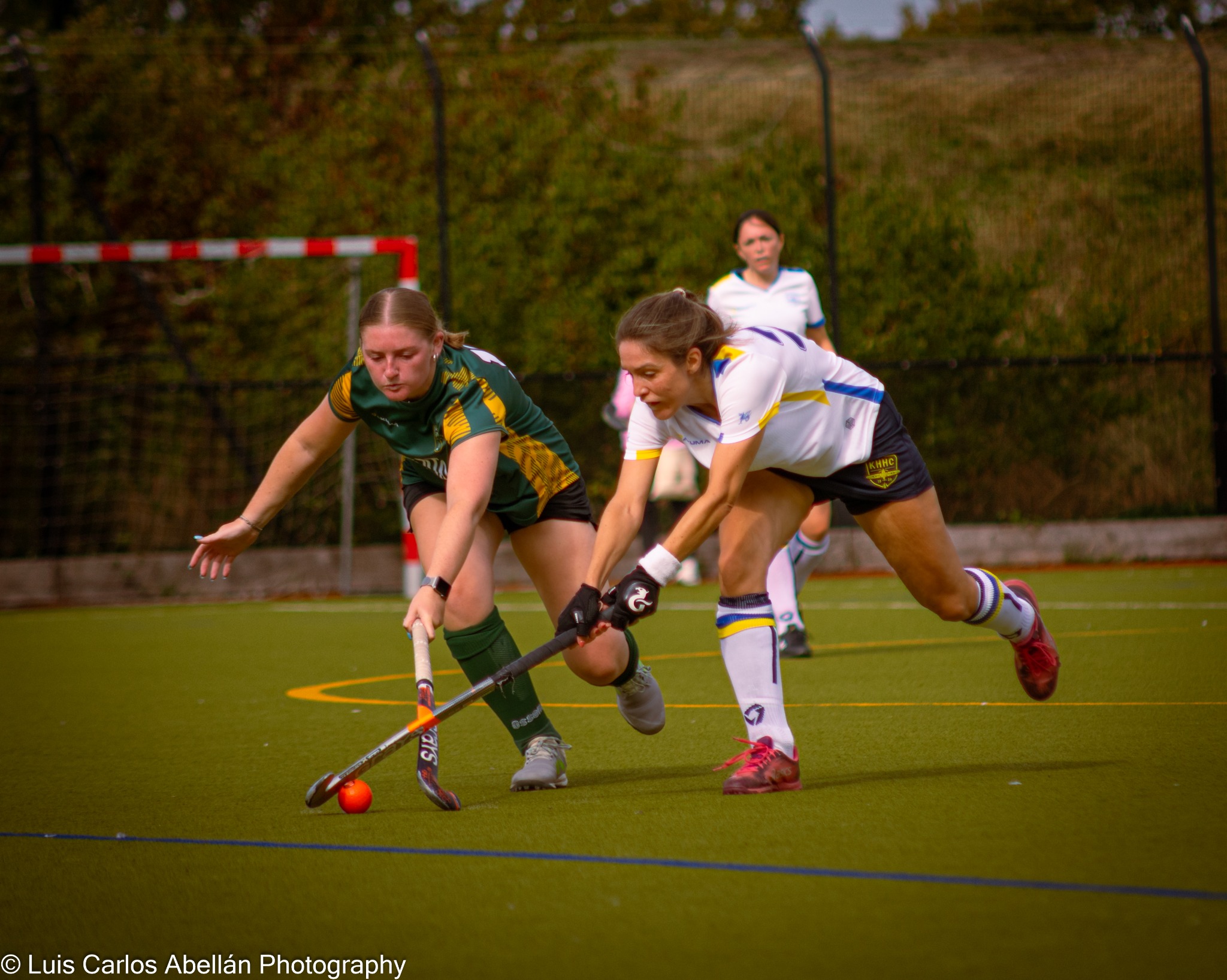 Players in white and green and yellow challenge for the ball at full stretch.