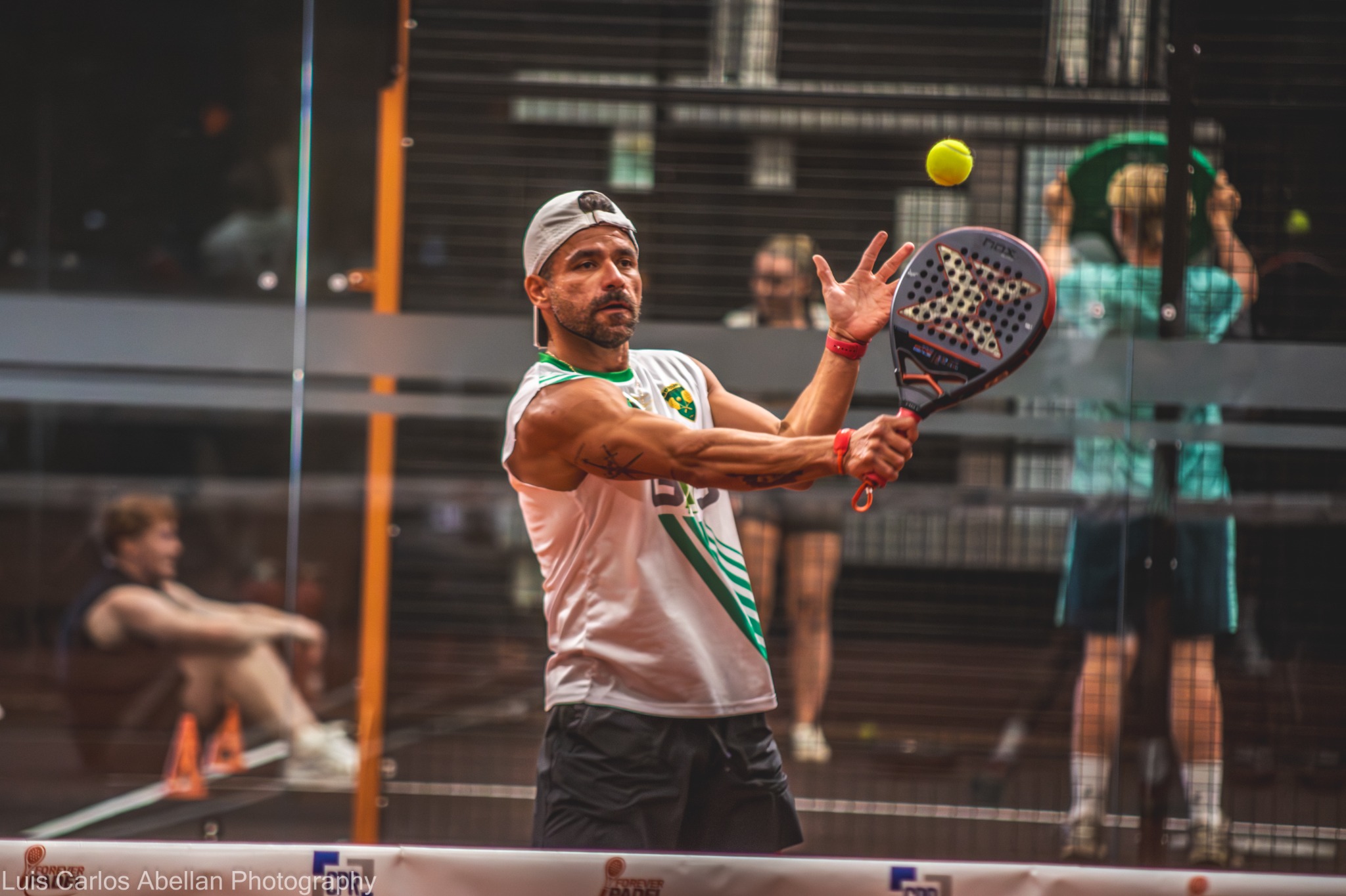 Padel player in a white and green shirt preparing a return