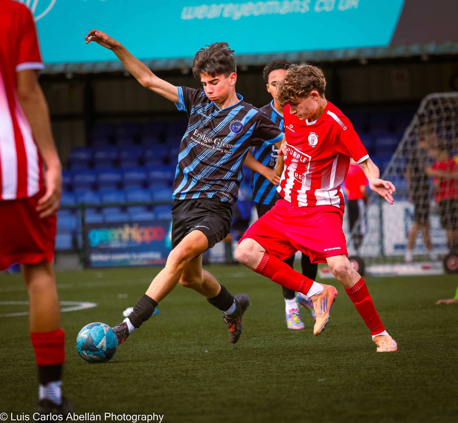Youth footballers in striped and red shirts contest the ball.