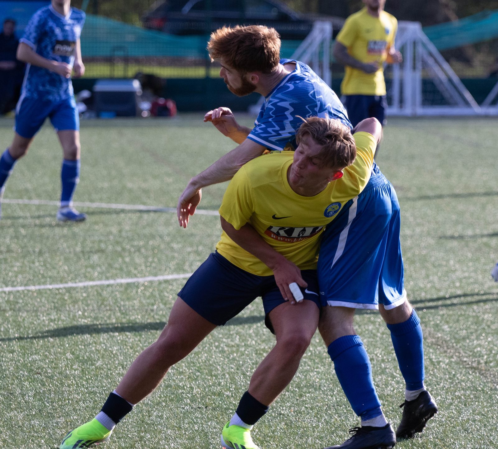 Two men footballers tussle for possession on the pitch.